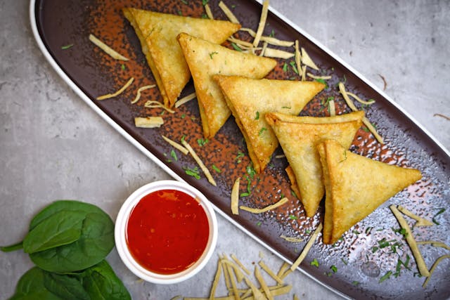 Five Kerala Samosas in a tray and Tomato sauce in a bowl next to it